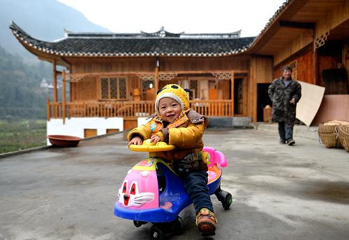 这是2014年1月12日,湖北省宣恩县水田坝村农民赵启新(右后)带着孙子在装修一新的吊脚楼前玩耍。2014年中央一号文件指出,加快编制村庄规划,推行以奖促治政策,以治理垃圾、污水为重点,改善村庄人居环境。