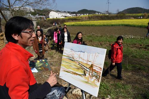 3月21日,一名画家在湖北省宜昌市夷陵区用画笔描绘盛开的油菜花